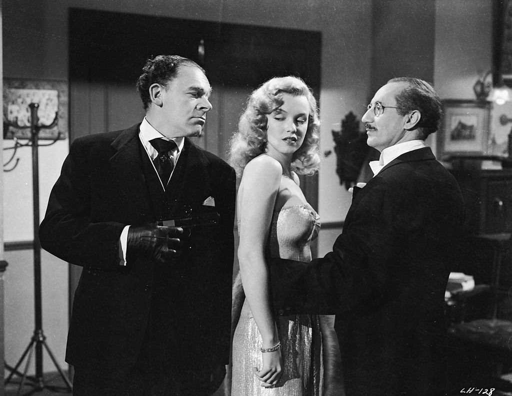 #1 Marilyn Monroe with Groucho Marx and fall foul of a man with a gun in a scene from ‘Love Happy’, 1949.