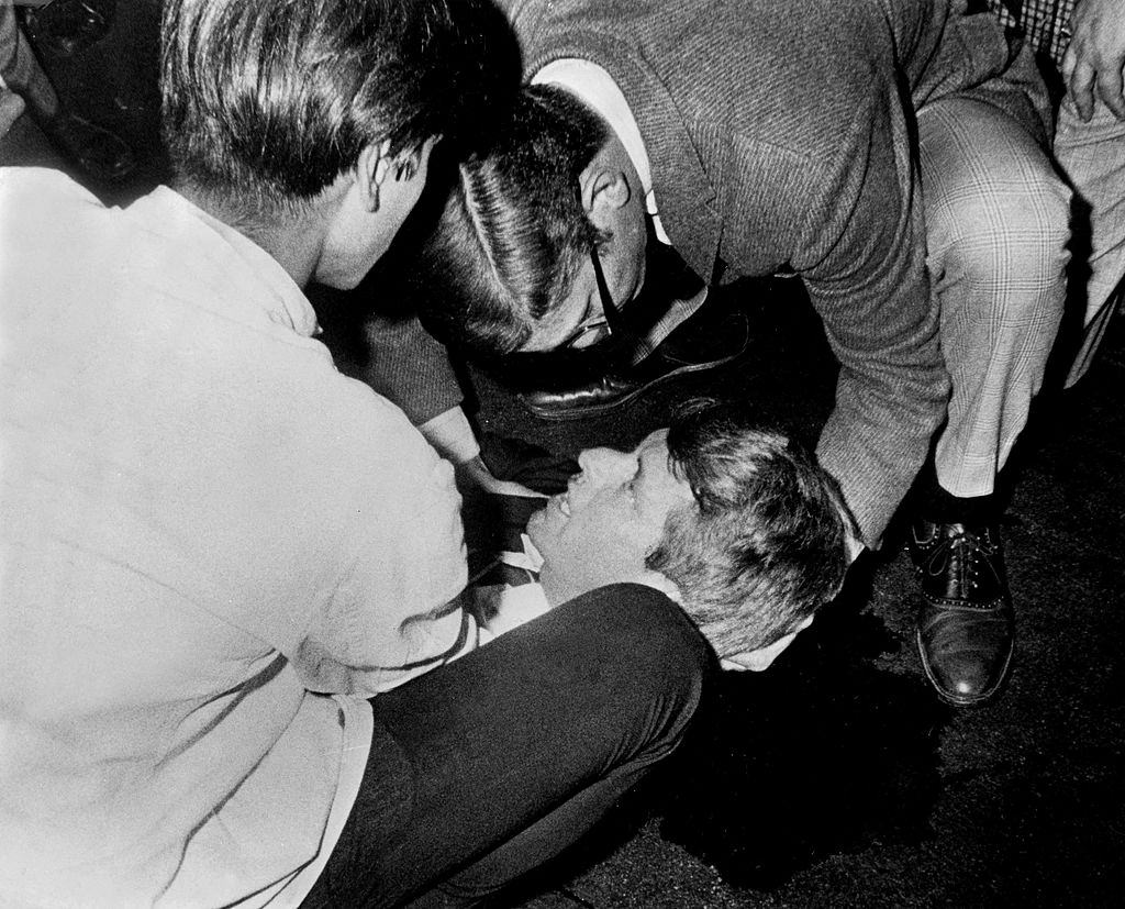 #8 Robert F, Kennedy lies on the floor, his shirt is opened and he looks up at people assisting him with a pool of blood beneath.