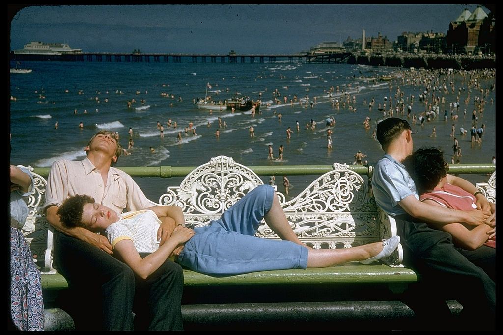 #9 Young woman lying on white wrought iron bench w. head resting in lap of boyfriend in Blackpool beach, 1955.