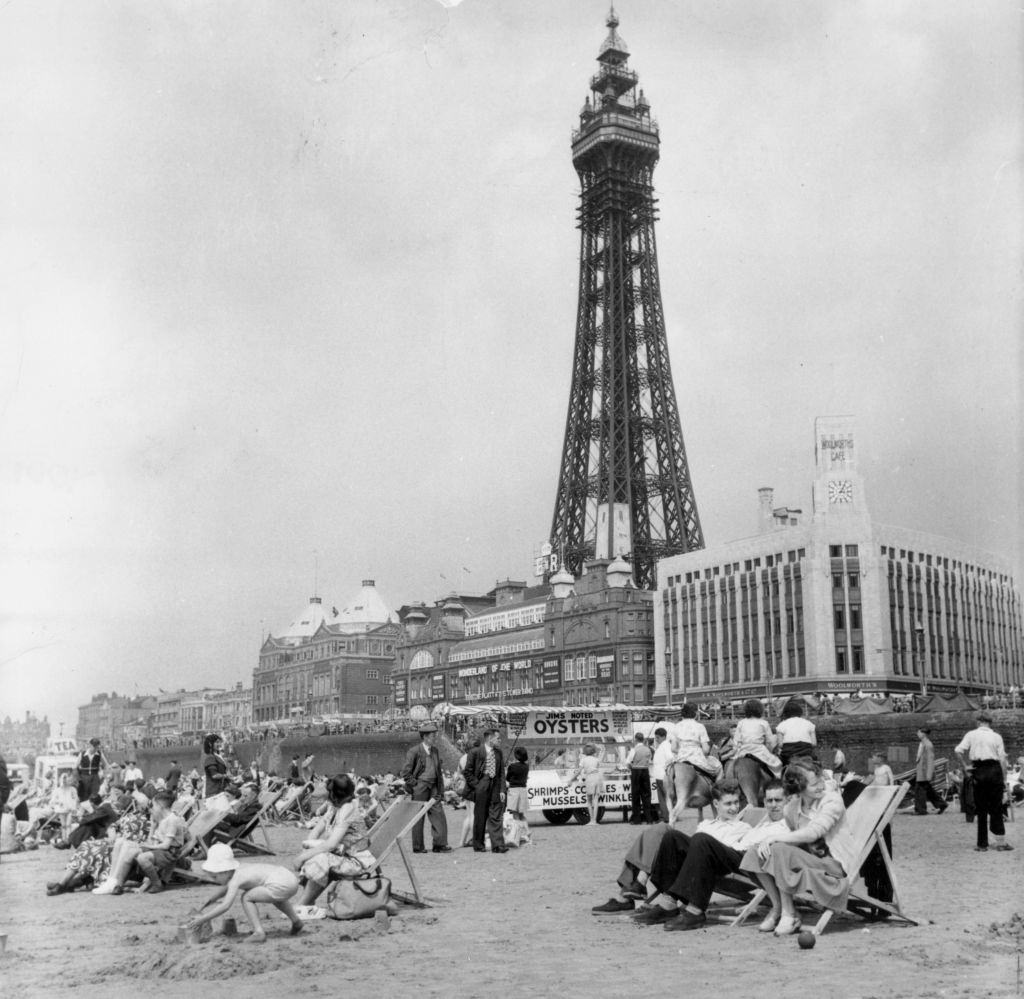 #22 Blackpool Tower behind holidaymakers relaxing on the beach of the famous Lancashire resort, 1953.