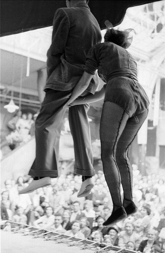 #23 A member of the audience, held by the seat of his pants by a performer, jumps up and down on a trampoline in front of the crowd at the famous seaside resort of Blackpool, 1953.
