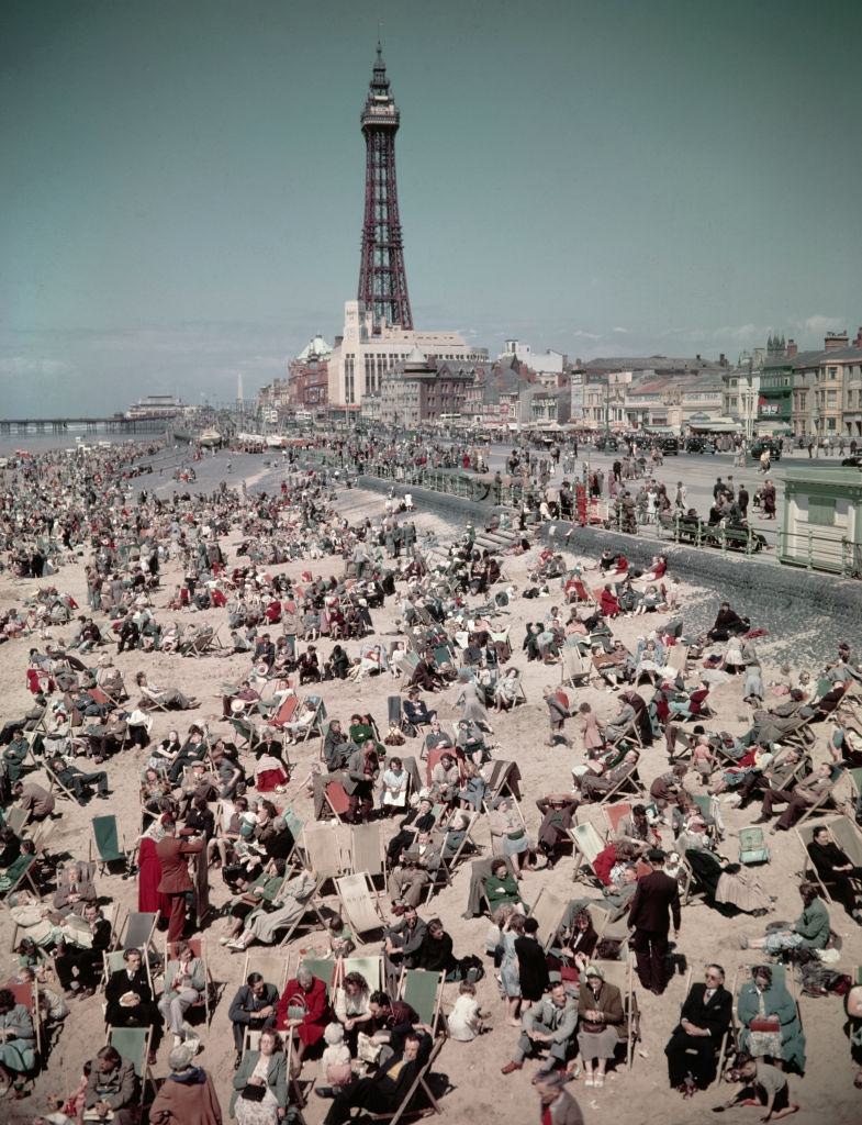 #27 Holidaymakers and visitors, many seated in deck chairs, enjoy a day on the beach at the seaside resort of Blackpool in Lancashire in August 1952.