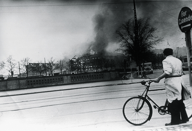 Cyclist looking at the burning Shellhouse (Getapo’s head quarter) after the RAF attack.. 18th April 1944.
