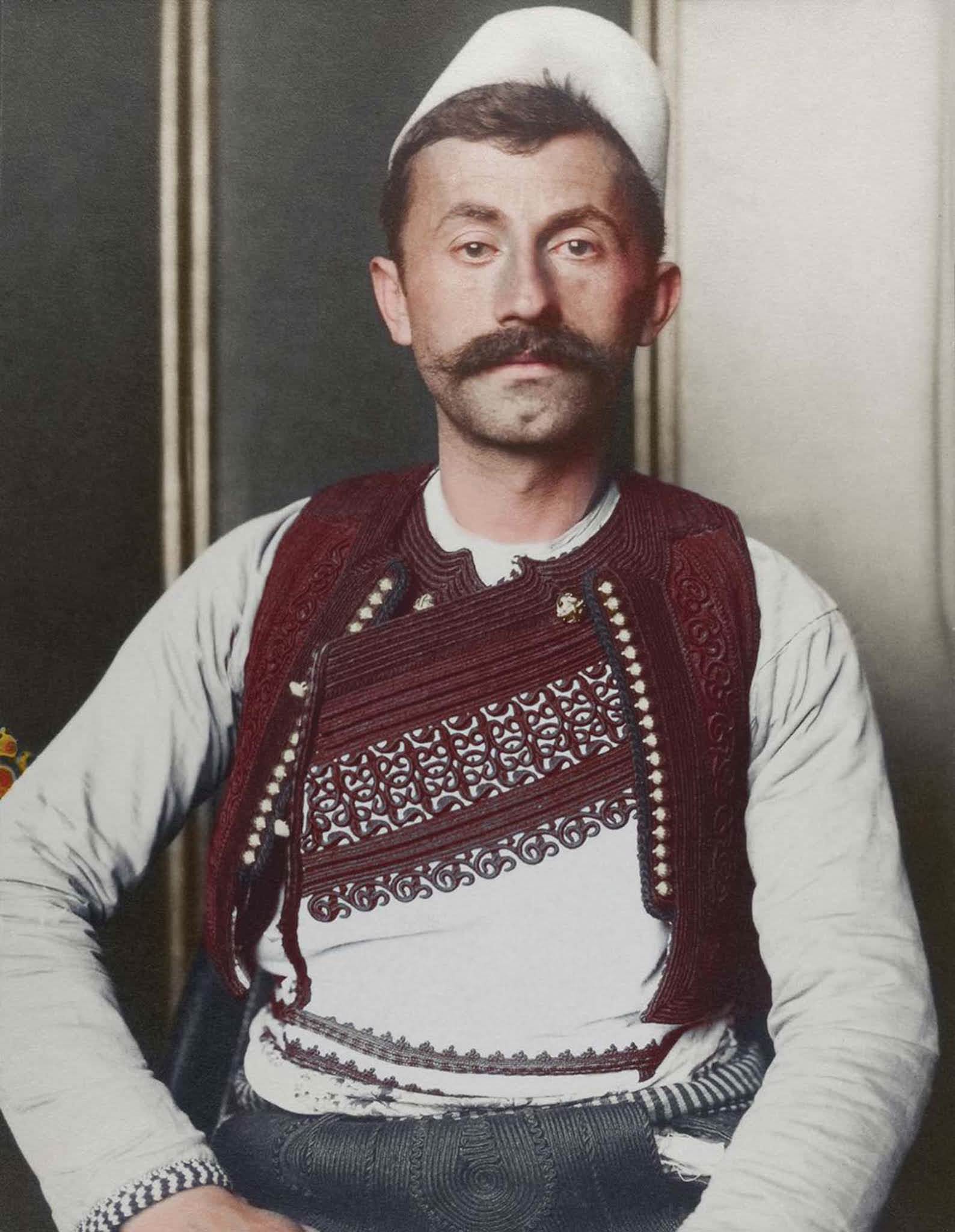 #8 Albanian soldier.” The truncated brimless felt cap is known as a qeleshe, whose shape was largely determined by region and molded to one’s head. The vest, known as a jelek or xhamadan, was decorated with embroidered braids of silk or cotton. Its color and decoration denoted the region where the wear