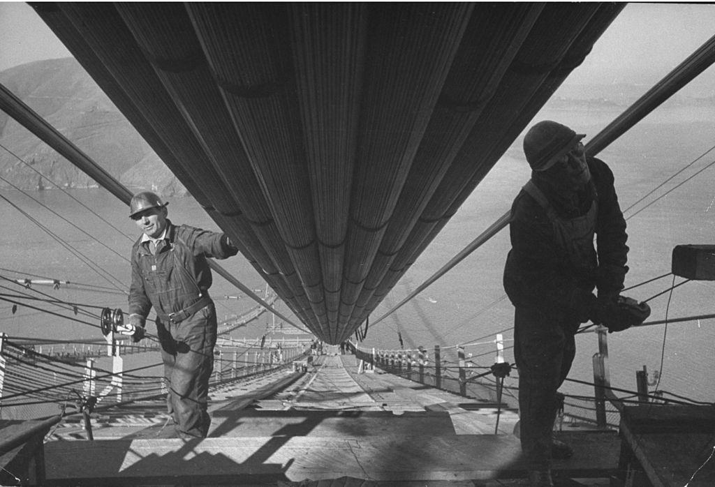 #40 Two workmen adding the last two strands to one of the two enormous cables to the structure that supports a 6-lane highway, during construction of the Golden Gate Bridge.