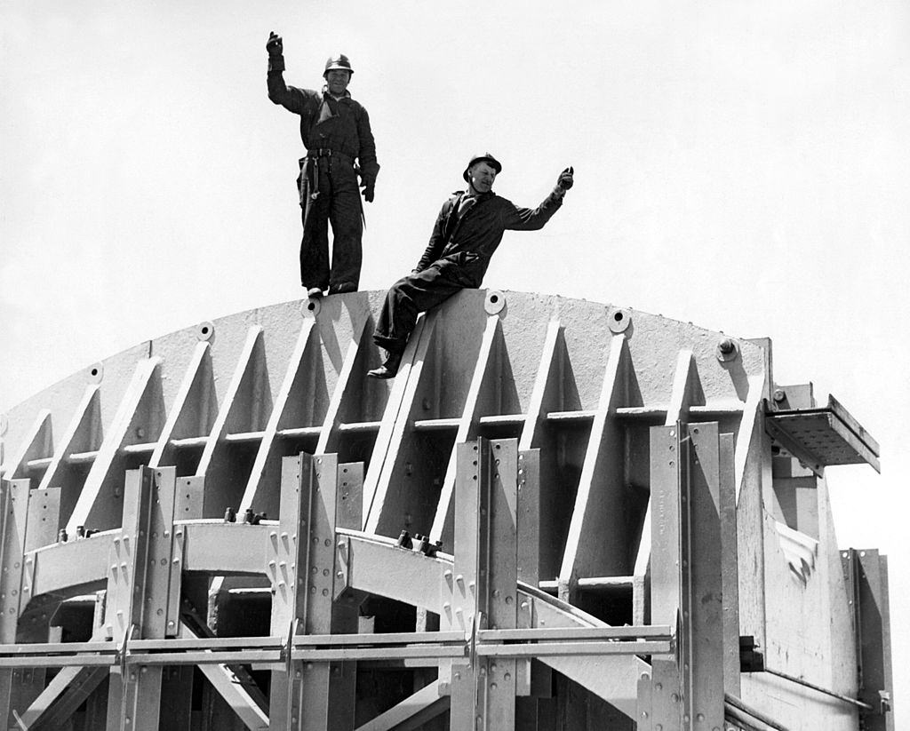 #12 The Golden Gate Bridge under construction with two workers on the saddle atop the Marin Tower, 746 feet above the water, San Francisco, California, 1934.