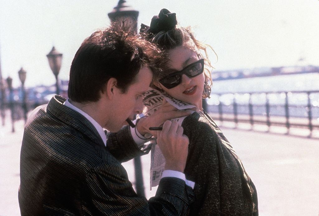 #41 Canadian actor Robert Joy writing a note on a newspaper resting on Madonna, 1985.
