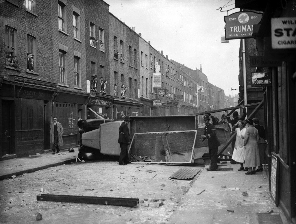 #10 Police remove an overturned lorry used as a barricade during the Communist-Fascist riots in Cable Street, 4th October 1936.