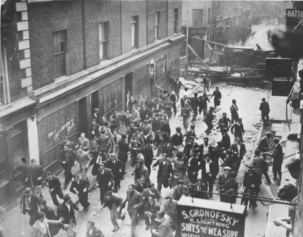 #18 A crowd of demonstrators fleeing as police break down a barricade in Cable Street, Aldgate, east London.