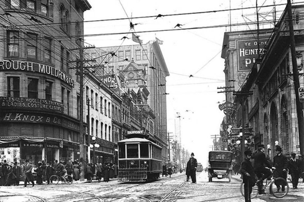 Cyclists occupy the edge of the frame at a busy Queen &; Yonge, 1910