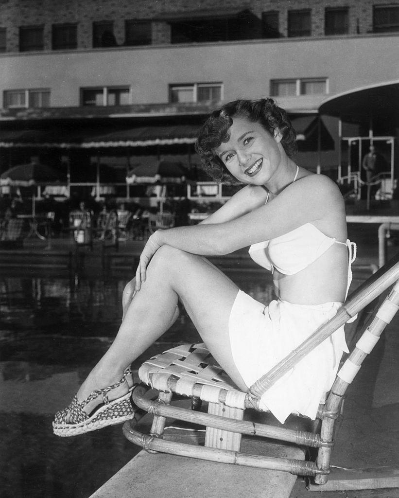 #52 Debbie Reynolds, smiling and sitting in a beach chair at the edge of a swimming pool, 1955.