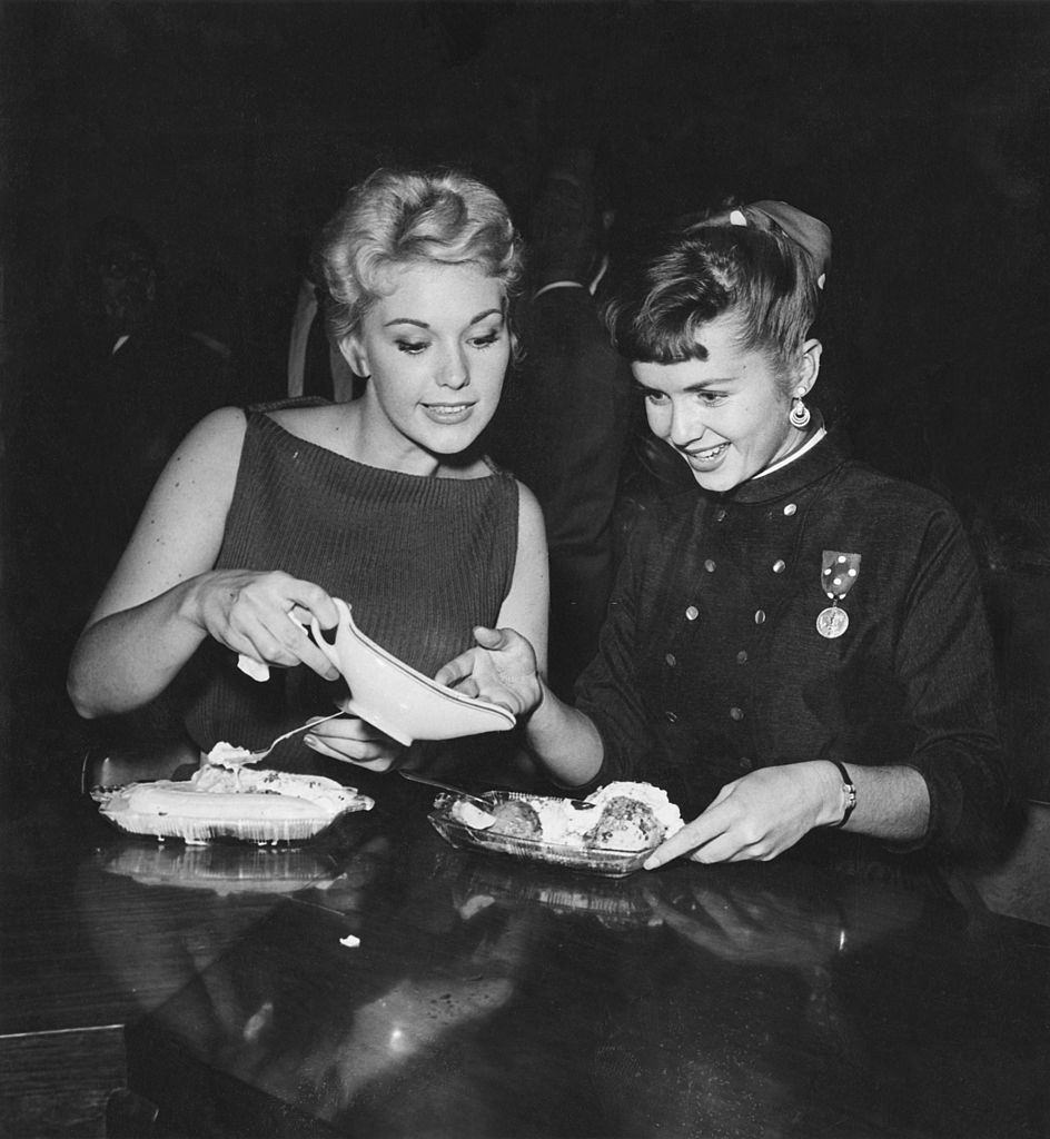 #57 Debbie Reynolds with Kim Novak enjoying ice cream sundaes at a Hollywood party, 1955.
