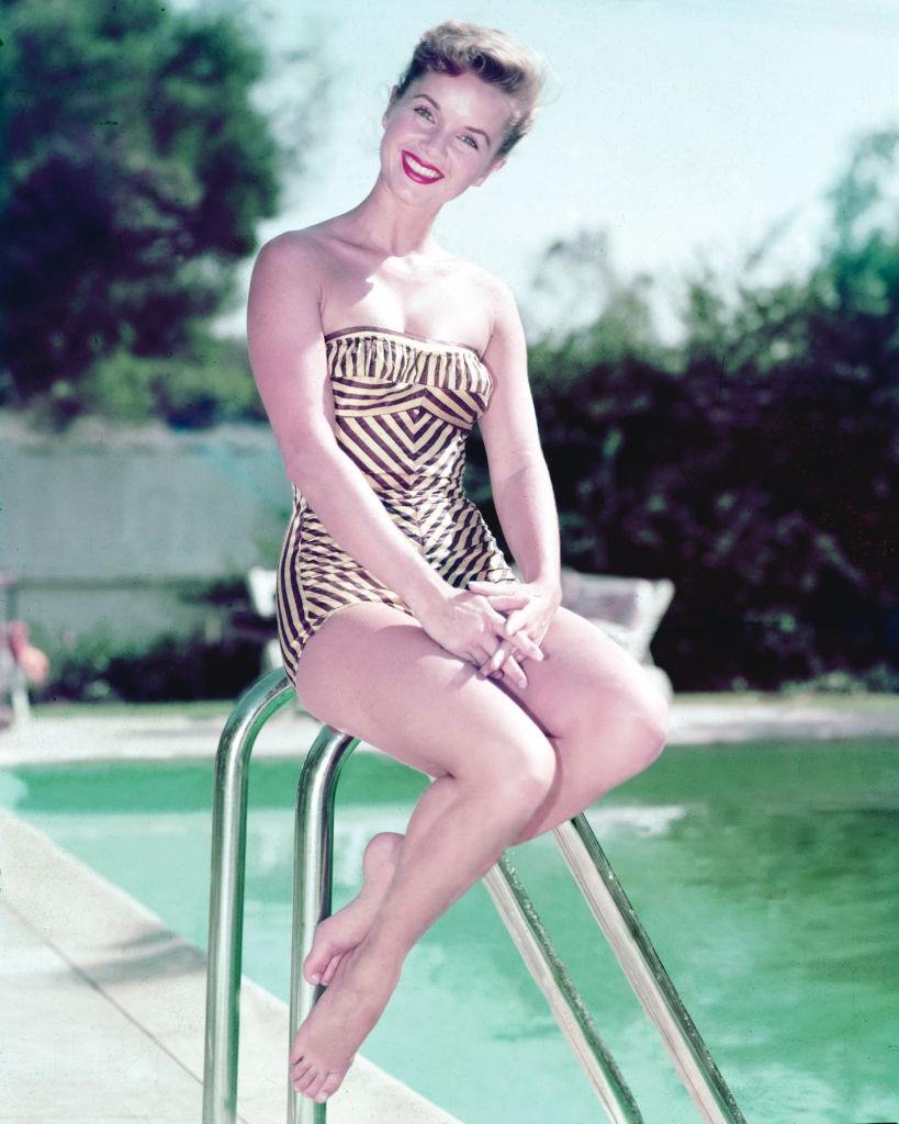 #21 Debbie Reynolds wearing a swimsuit, sitting beside a swimming pool, 1955.