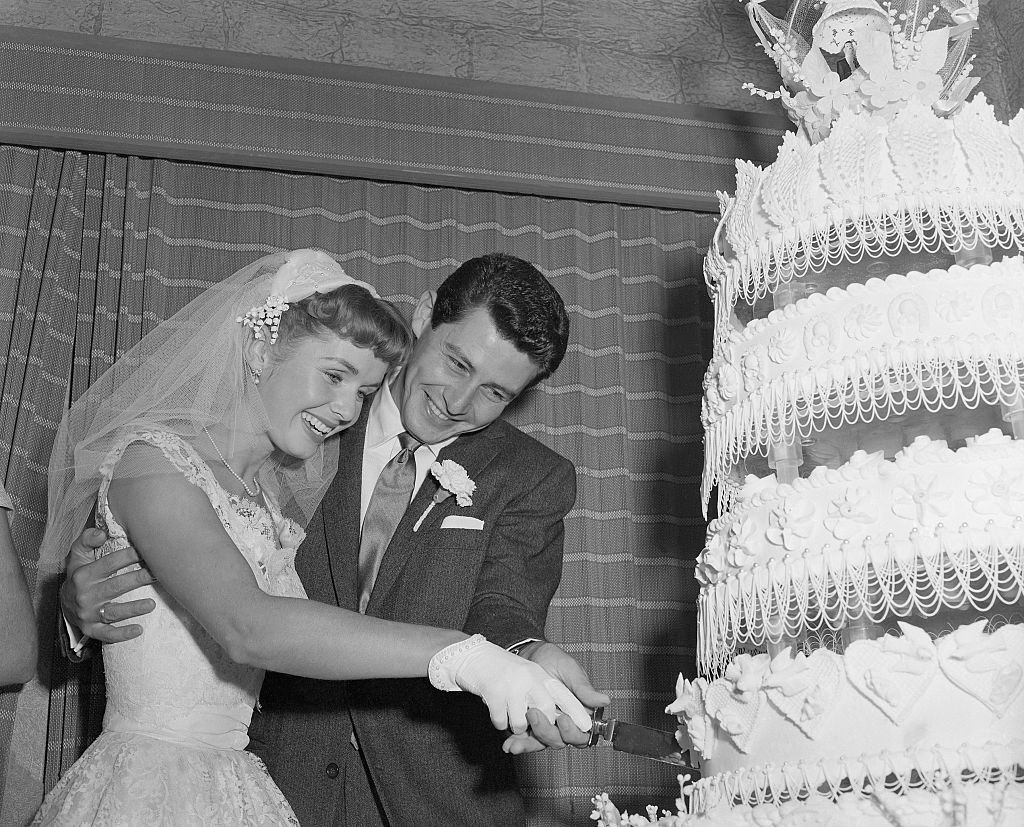 #70 Debbie Reynolds and singer Eddie Fisher cut their towering wedding cake after they were married at Liberty, 1955.