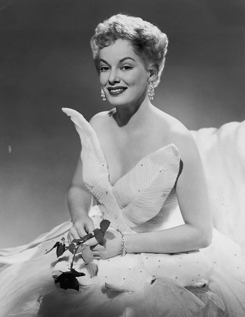 #9 Faye Emerson wearing a leaf-patterned white gown, and holding a rose, 1948.