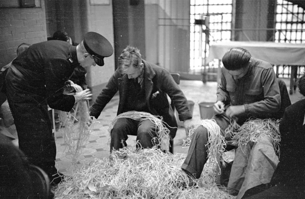 #7 A prison officer supervising prisoners who are untying knots in Post Office string at Strangeways Prison.