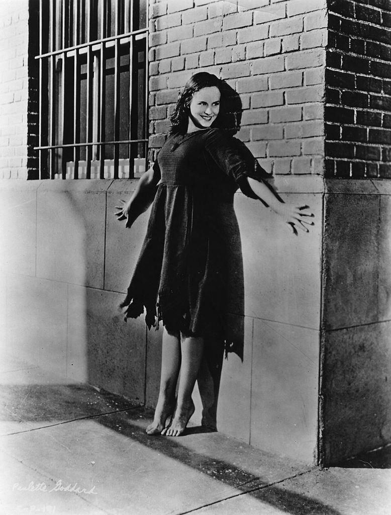 #39 Paulette Goddard standing barefoot and on tiptoe in front of a barred window, 1936.