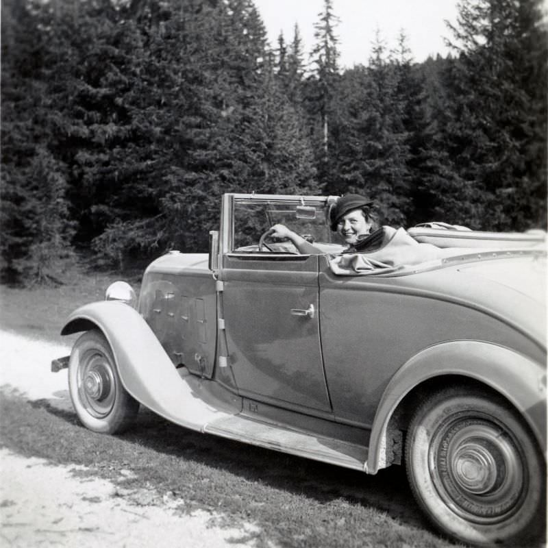 A cheerful lady posing in the driver’s seat of a Renault Monaquatre Cabriolet-Spider convertible on a dirt road in the countryside, 1935