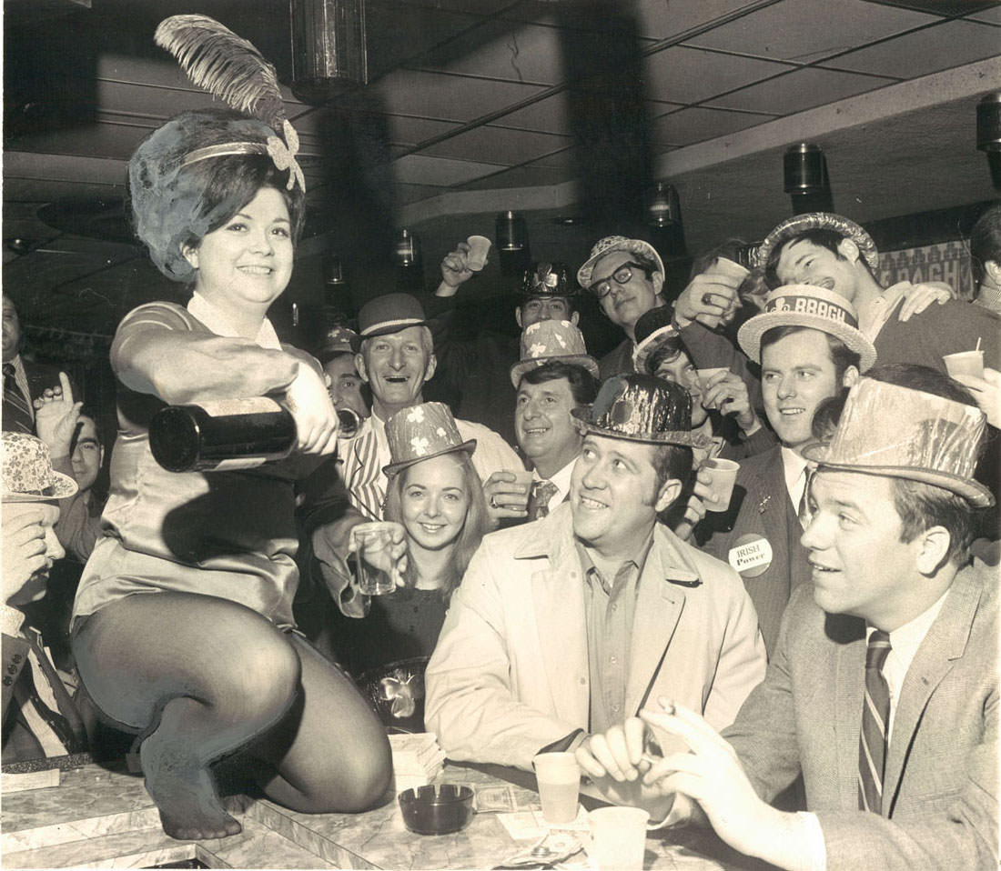 #1 Susie Cook pours a stiff dram of usquebaugh in Sweeney’s bar amid a crowd of St. Patrick’s Day revelers smiling with happy Irish eyes. March 18, 1970.
