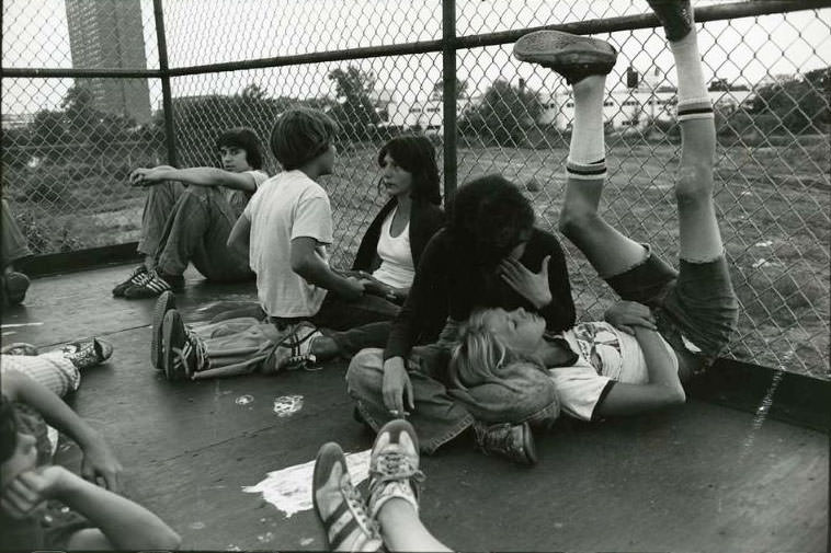 #3 Five teenagers sitting in a fence enclosed area. In the background is the Rindge Towers Housing Project, Jefferson Park, 1973