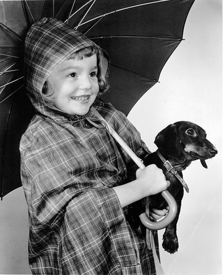 #22 Tuesday Weld holding dog in rain gear in publicity portrait, 1948.
