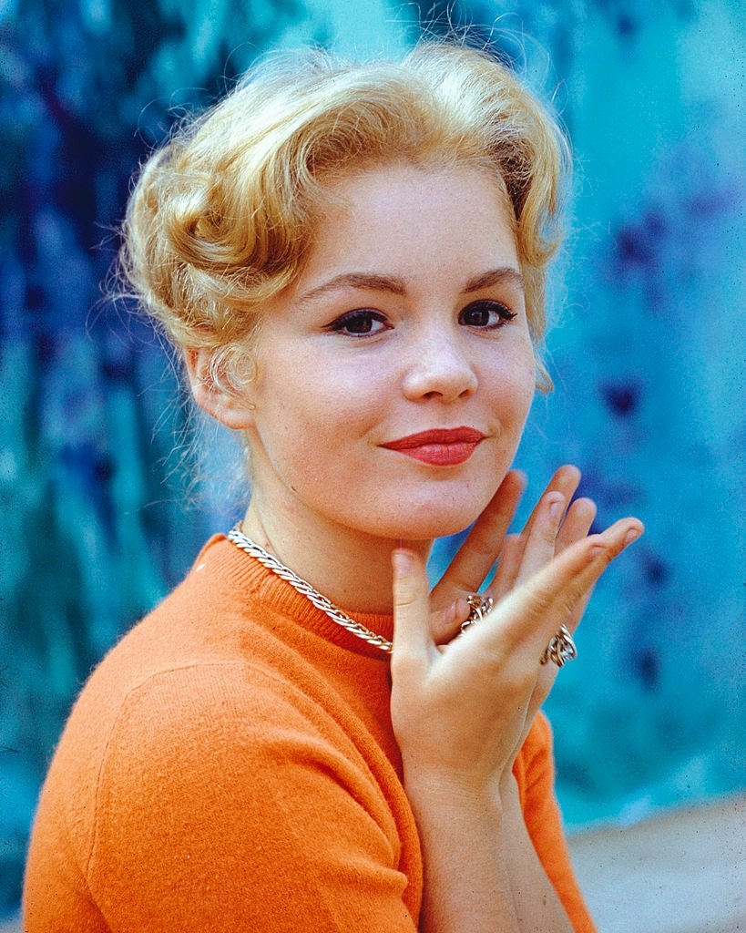 #65 Tuesday Weld wearing an orange top and a gold chain around her neck, 1965.