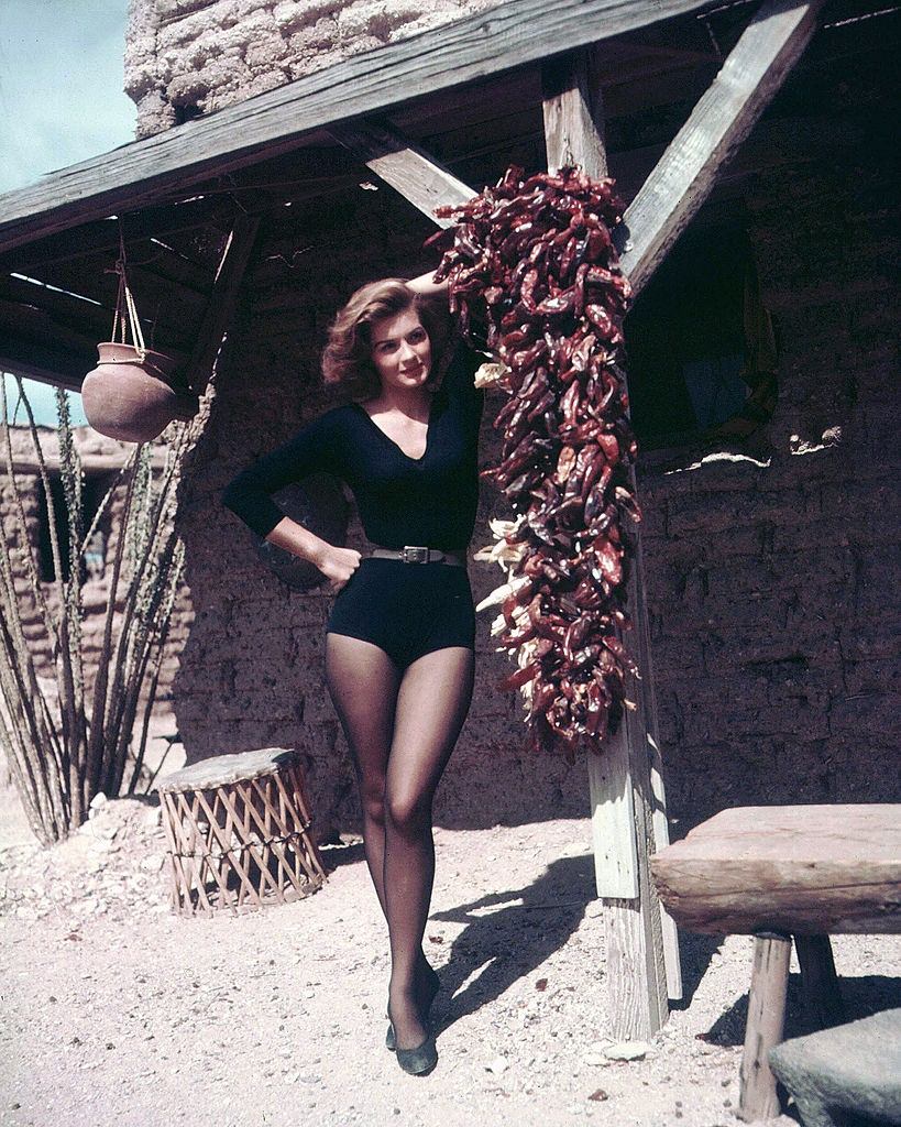 #20 Angie Dickinson posing beside a bundle of dried chillies hanging on the set of ‘Rio Bravo’, 1959.