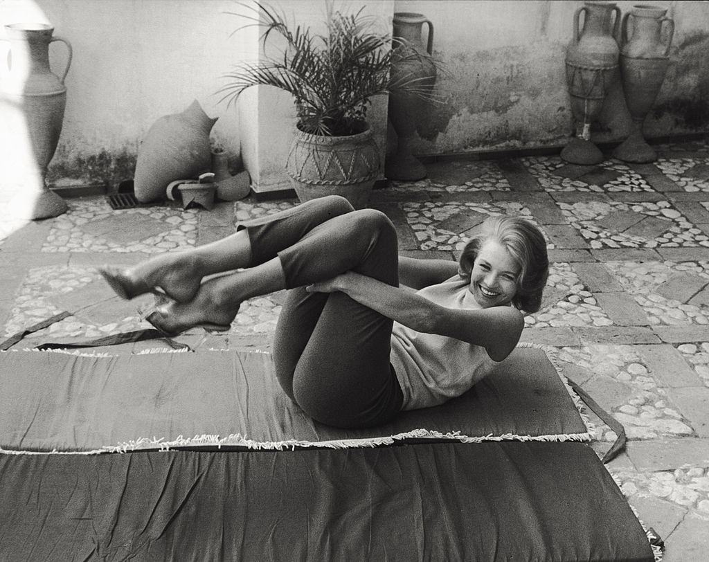 #51 Angie Dickinson moving her legs to her chest lying on a mat on a terrace, 1961.