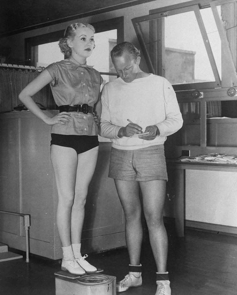 #12 Betty Grable is weighed by her personal trainer, 1936.
