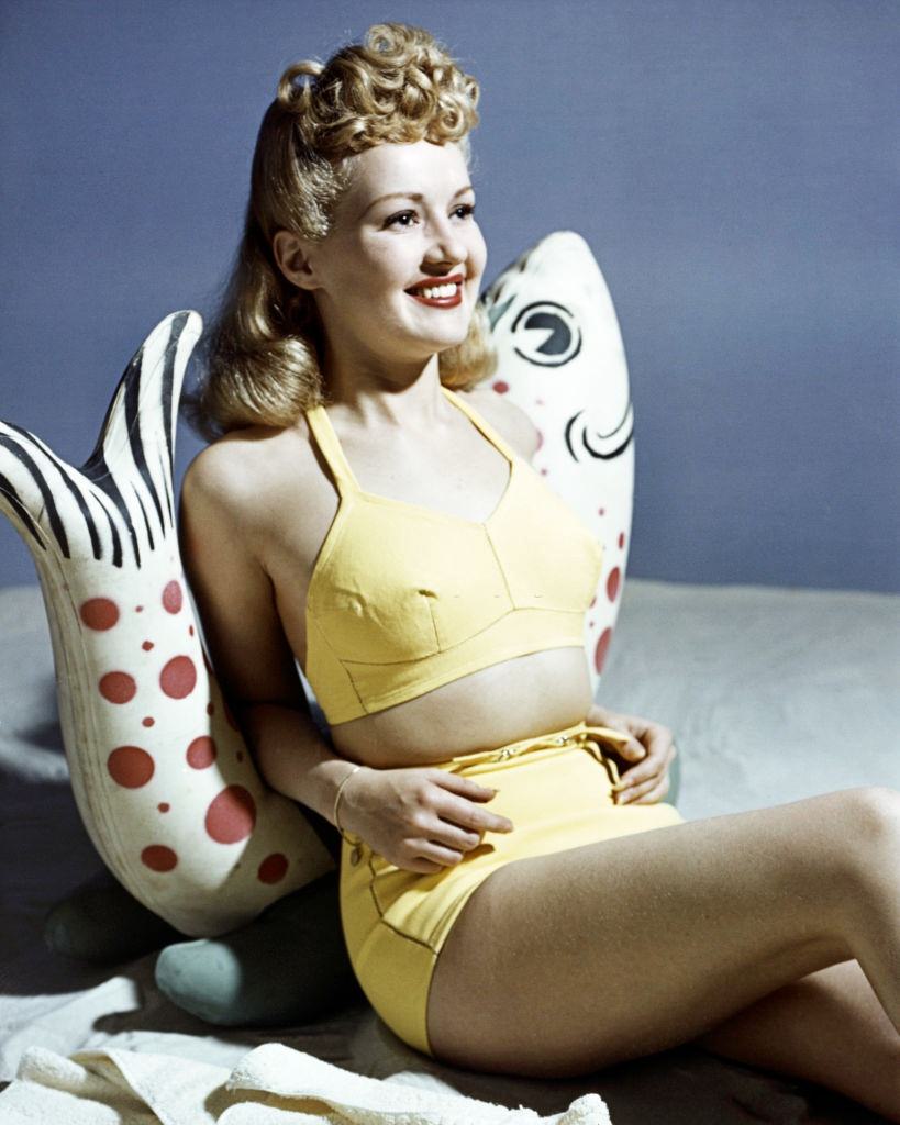 #33 Betty Grable wearing a yellow bikini as she leans against a fish ornament, 1940.
