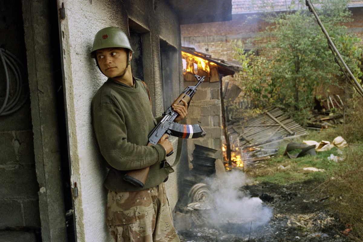 #17 A Serbian soldier takes cover by a burning house in the village of Gorica, Bosnia-Herzegovina, on October 12, 1992.