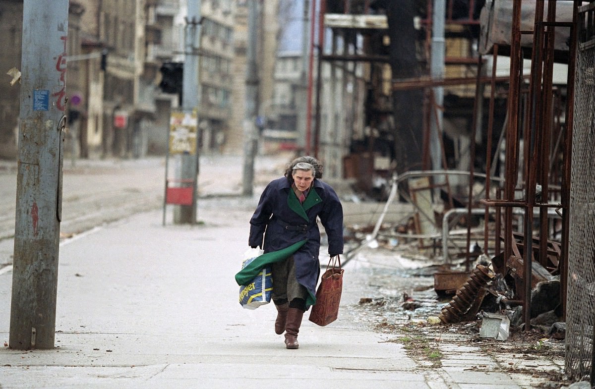 #20 Bosnian woman rushes down an empty sidewalk past war-destroyed shops in one of the worst sections of the so-called “Sniper Alley.”