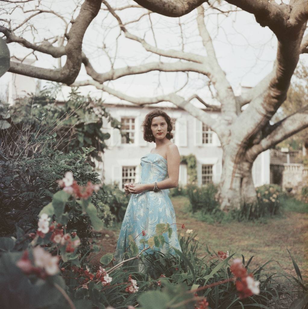#20 An unidentified woman stands in a garden wearing a strapless blue dress, Bermuda, 1957.