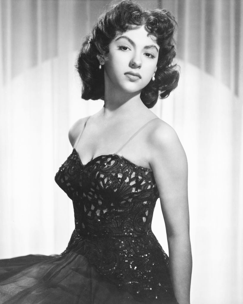 #37 Rita Moreno wearing a black thin strap dress in a studio portrait, 1955.