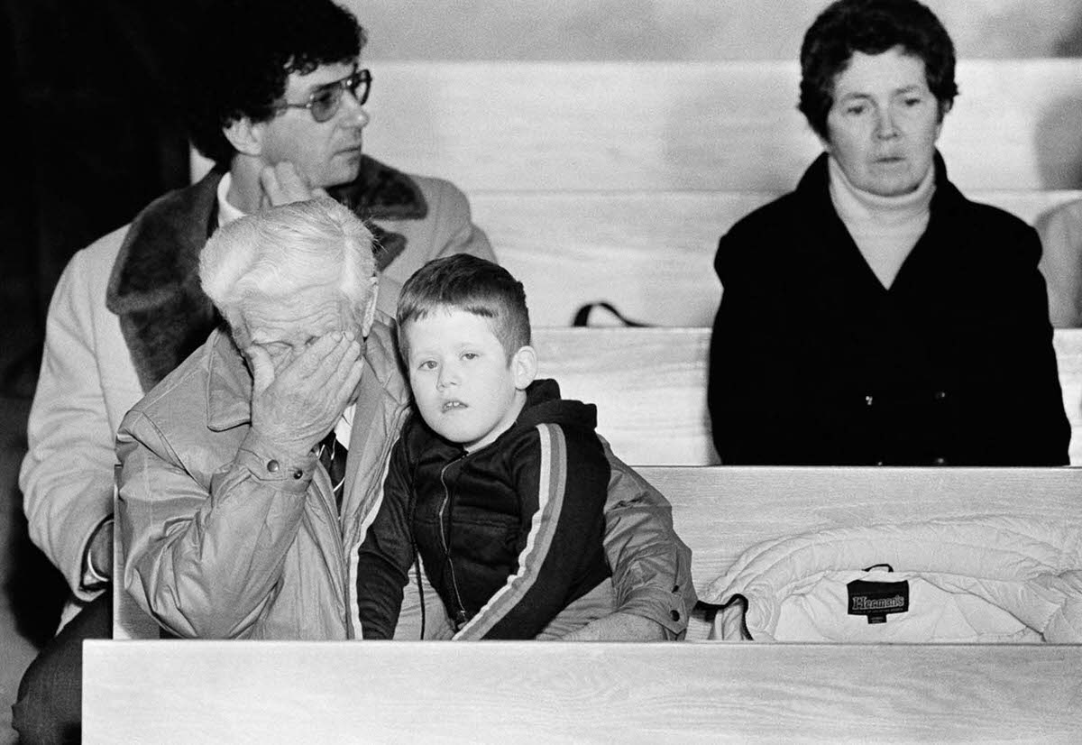 #18 Billy Gifford rubs his eyes while holding his grandson Jimmy Stillman, 8, during a memorial service for Christa McAuliffe at a church in Concord, New Hampshire. Jan. 29, 1986.