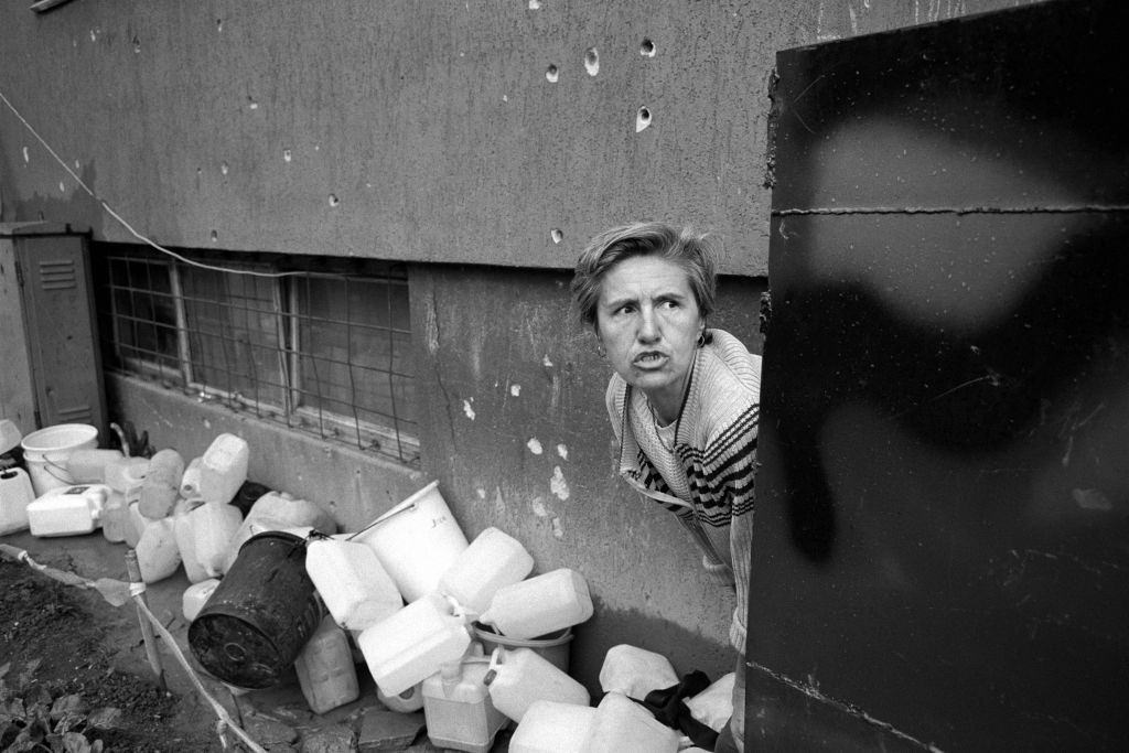 #64 A frightened woman collects water at a stand pipe during an exchange of gunfire between Bosnian and Serbian fighters, July 1992.