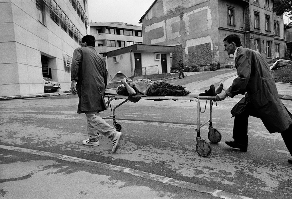 #48 Porters from Kosovo Hospital rush a man wounded by a shell to the emergency room, during the Siege of Sarajevo, Bosnia, July 1992.