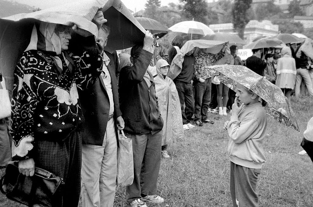 People shelter from the rain under their umbrellas during filming of ‘Welcome to Sarajevo’ starring Woody Harrelson, 1994.