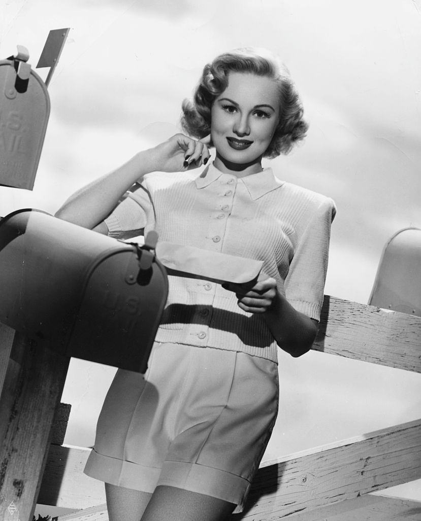 #6 Virginia Mayo leaning on a fence and reading mail from a mailbox, 1945.