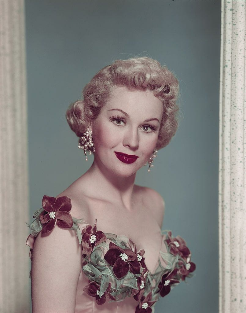 #9 Virginia Mayo wearing elaborate pearl ear rings and a corset dress, 1950.