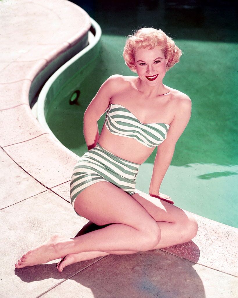 #1 Virginia Mayo wearing a green-and-white striped bikini, posing at the edge of a swimming pool, 1945.