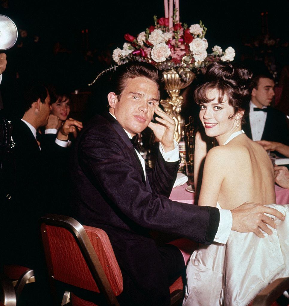 #20 Warren Beatty and Natalie Wood look over their shoulders while seated together at a formal event, 1961.
