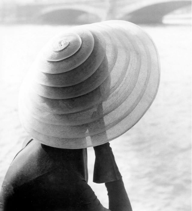 #13 Model wearing hat by Jacques Fath sitting by the river Seine, photo by Regina Relang, Paris, 1951