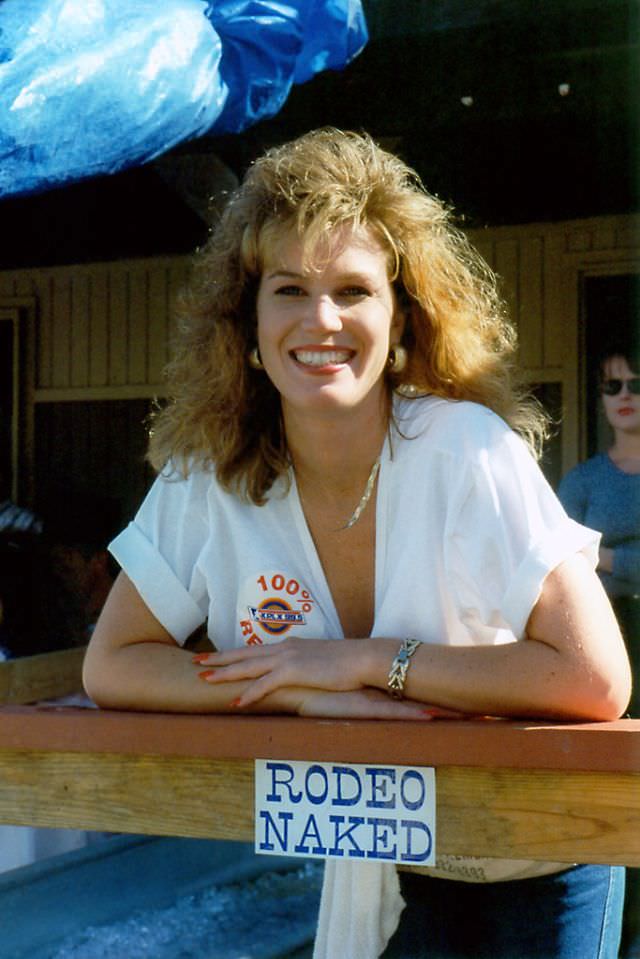 #20 A woman working a drink booth poses by a sign reading “Rodeo Naked” during a festival, possibly the Chisholm Trail Roundup, Fort Worth Stockyards, June 1994
