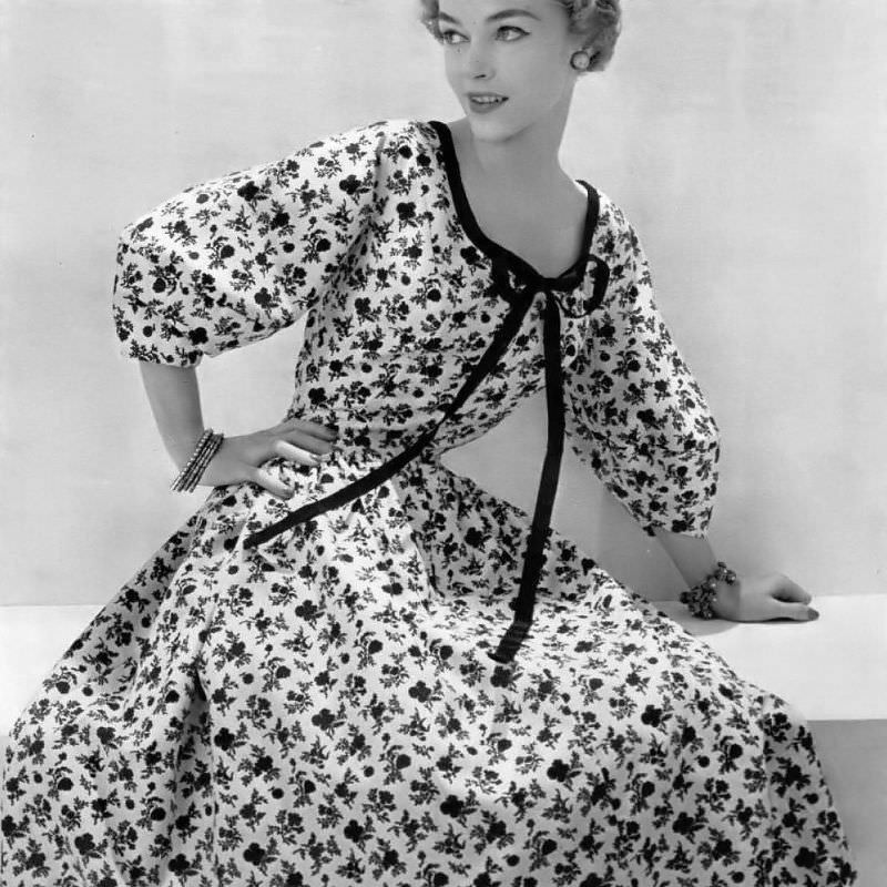 #19 Joan Olson in a romantic cream and black floral print dress bordered in black gros-grain ribbon by Mad Carpentier, 1954