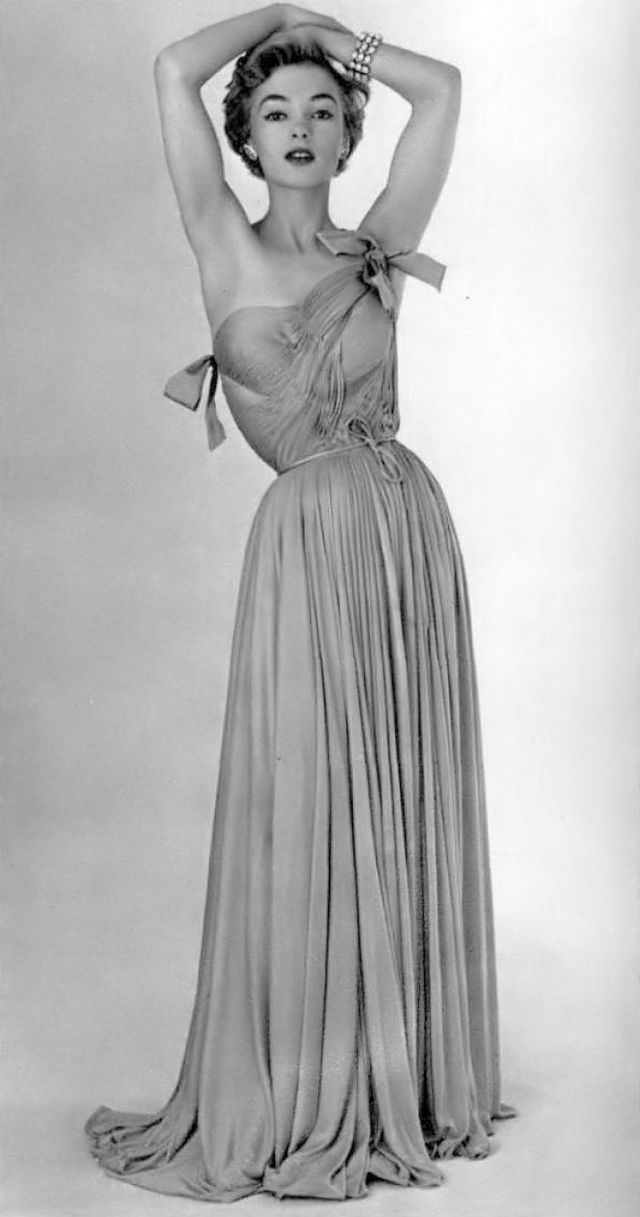 #28 The draped bodice sculpts this jersey gown with pale pink silk, skirt falls loosely, two satin bows adorn the bodice worn by model Joan Olson, by Grès, 1954
