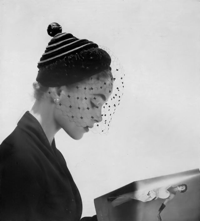 #3 Joan Olson in black velvet and satin spiral that wraps to a point on this small hat with voilette by Le Monnier, 1952