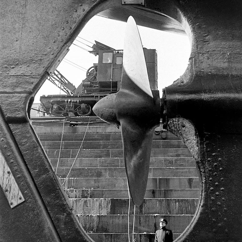 #7 A Naval officer — dwarfed by the vessel in his view — gazes at a cruiser’s propeller at the Brooklyn Navy Yard, 1941.