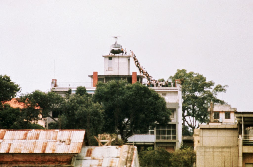 #42 A CIA employee (probably O.B. Harnage) helps Vietnamese evacuees onto an Air America helicopter from the top of 22 Gia Long Street, a half mile from the U.S. Embassy, 29 Apr 1975, Saigon, South Vietnam.