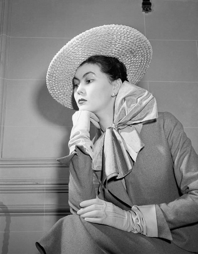 #5 Alla in a simple gray suit with a checked blouse featuring a huge bow at the throat, natural straw sailor hat tilts over one eye, 1949